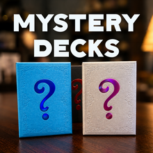 Two mystery decks of cards standing upright on a wooden table, one blue and one white, each with a large question mark on the front. Large white text at the top reads 'MYSTERY DECKS' against a blurred festive background with warm lights.