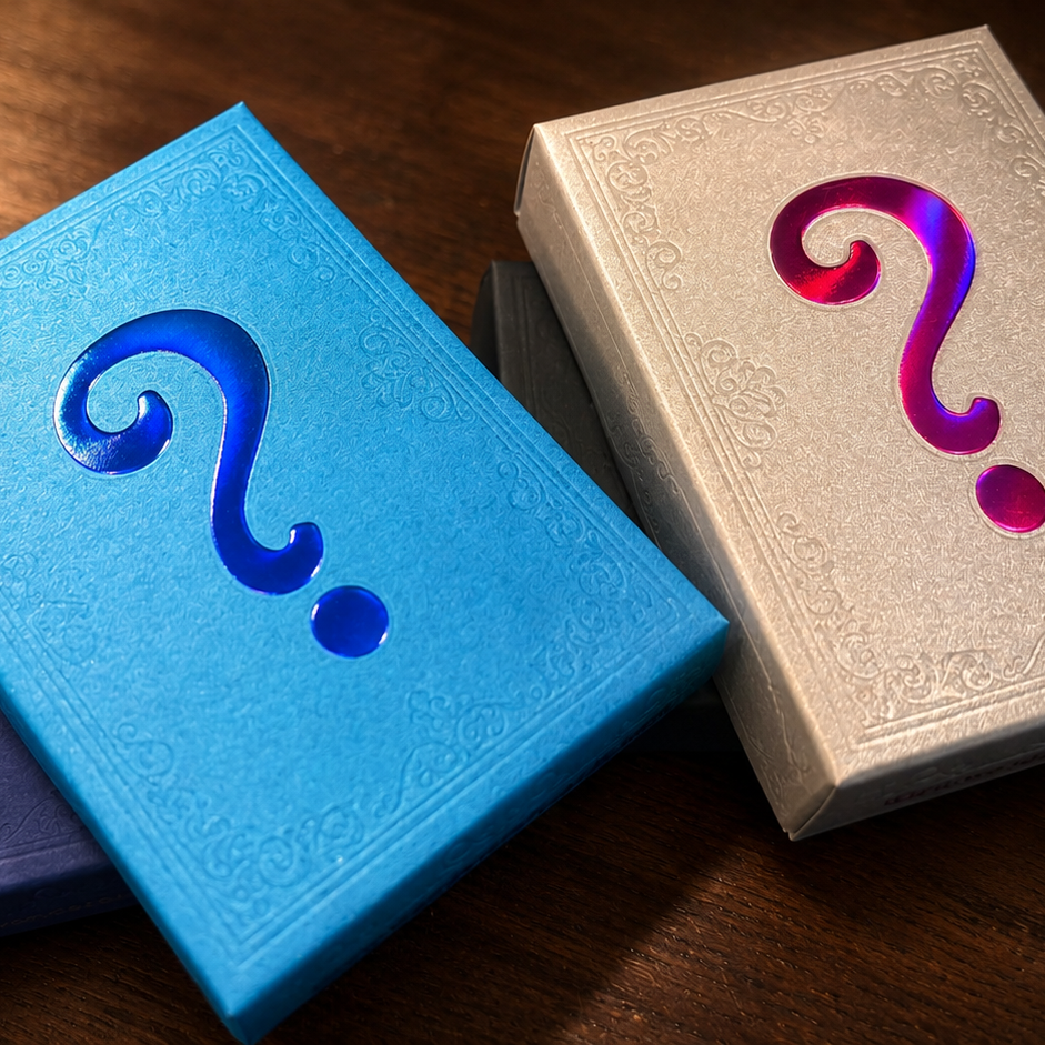 Three embossed book-like boxes with question marks on a wooden surface: a bright blue box in front, a cream box to the right with a purple-pink question mark, and a dark blue box behind the blue one.